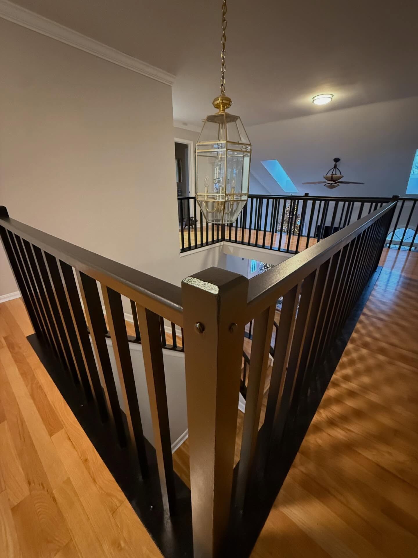 Interior landing with dark wooden railing, hardwood floor, and hanging lantern light in a bright hallway