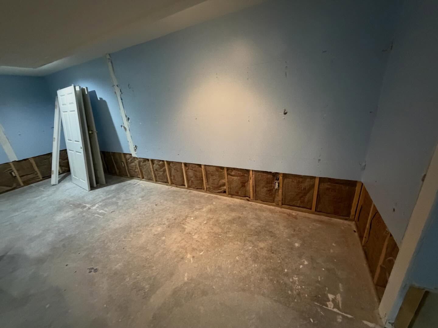 Empty room under renovation with blue walls, unfinished lower wall, and a concrete floor.