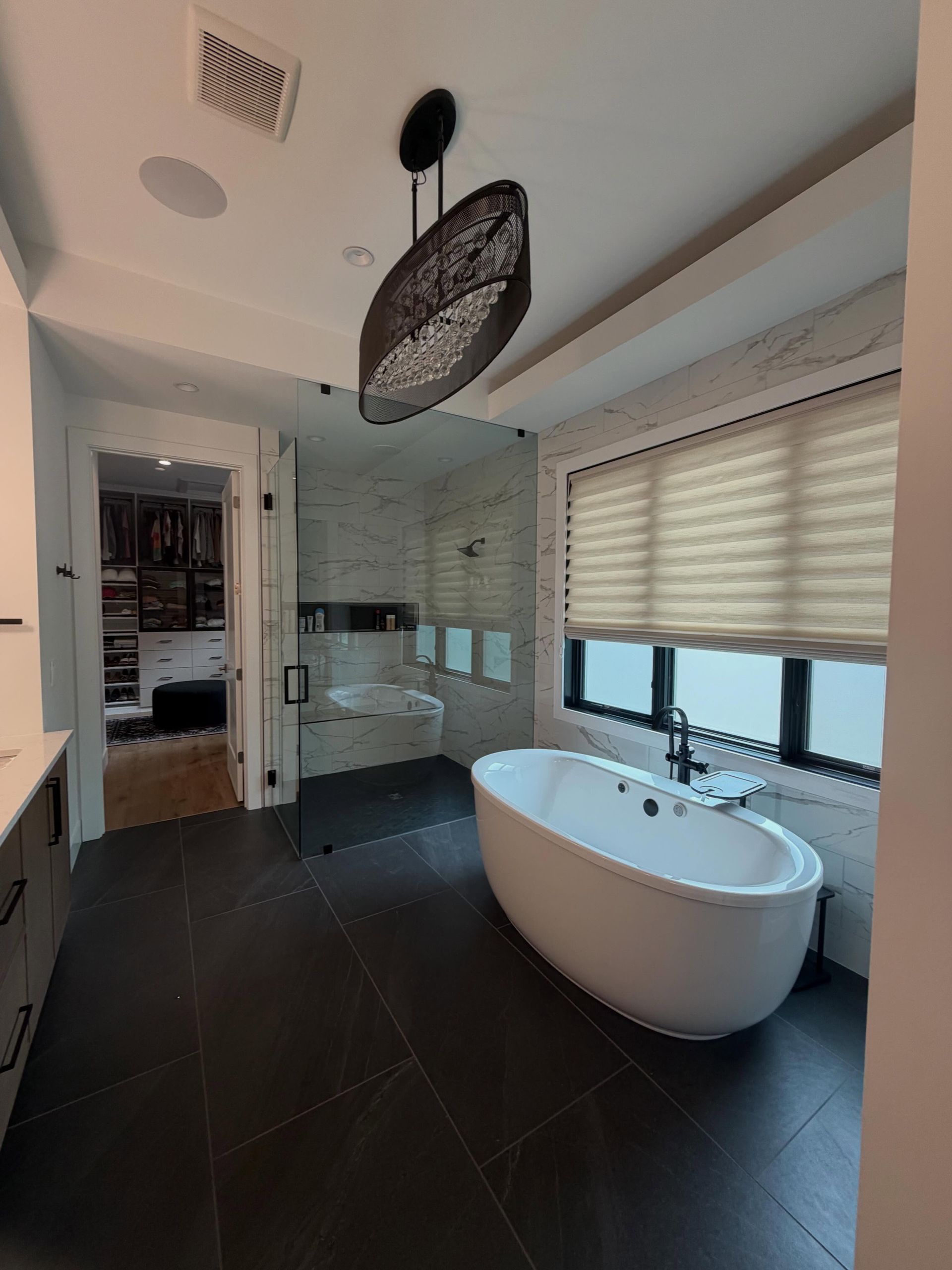 Modern bathroom with freestanding tub, glass shower, and large window blinds