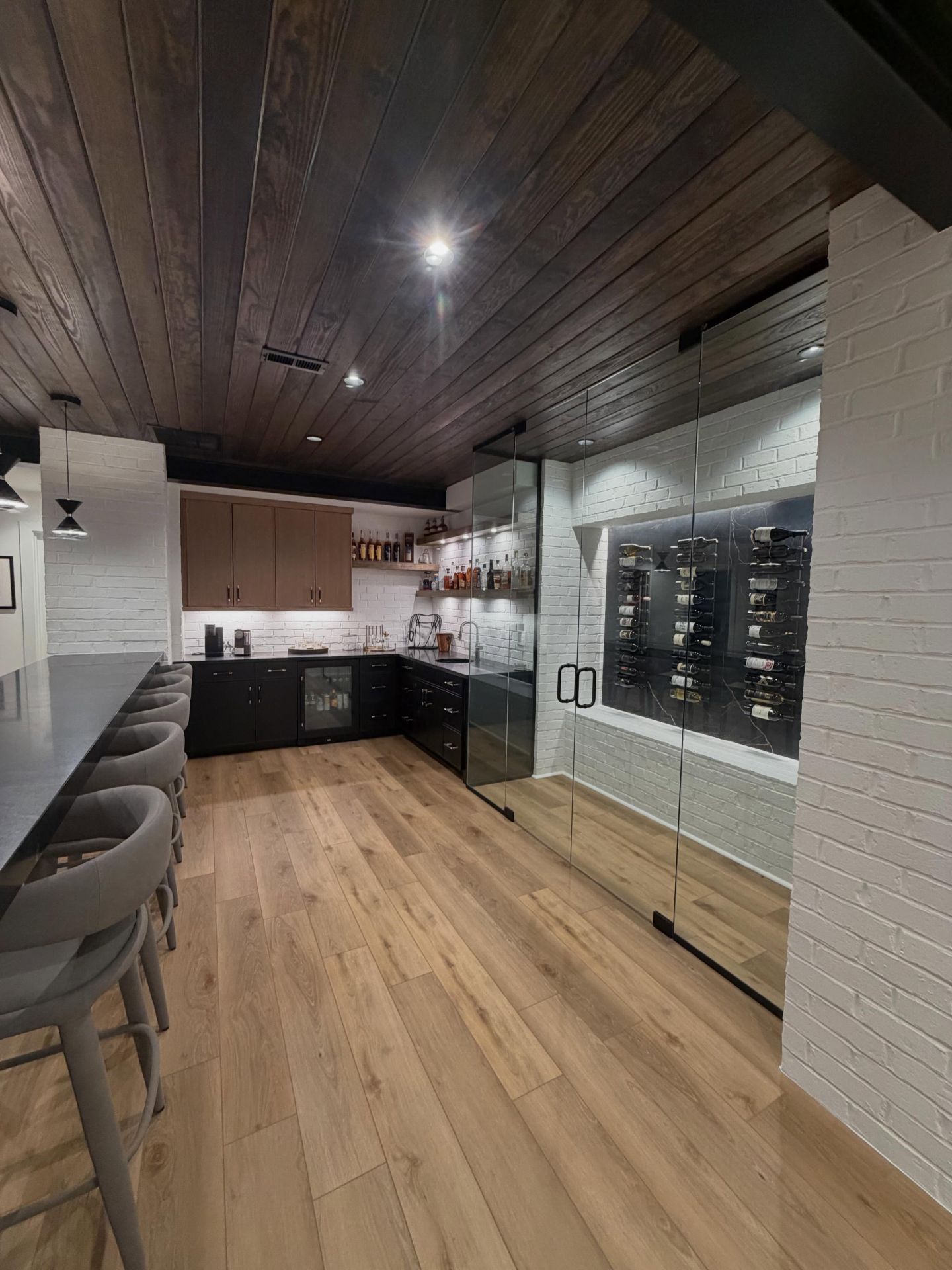 Modern bar interior with wood ceiling, white brick walls, black counters, and barstools along one side