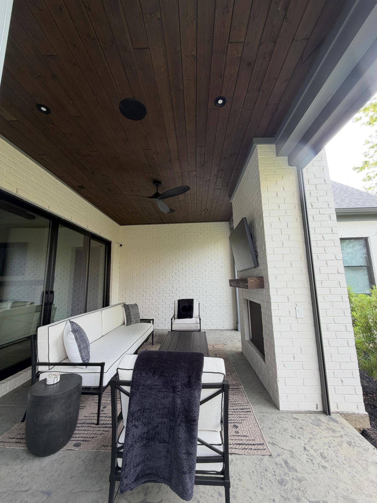 Covered patio with white brick walls, wood ceiling, and outdoor seating with a table and chairs.