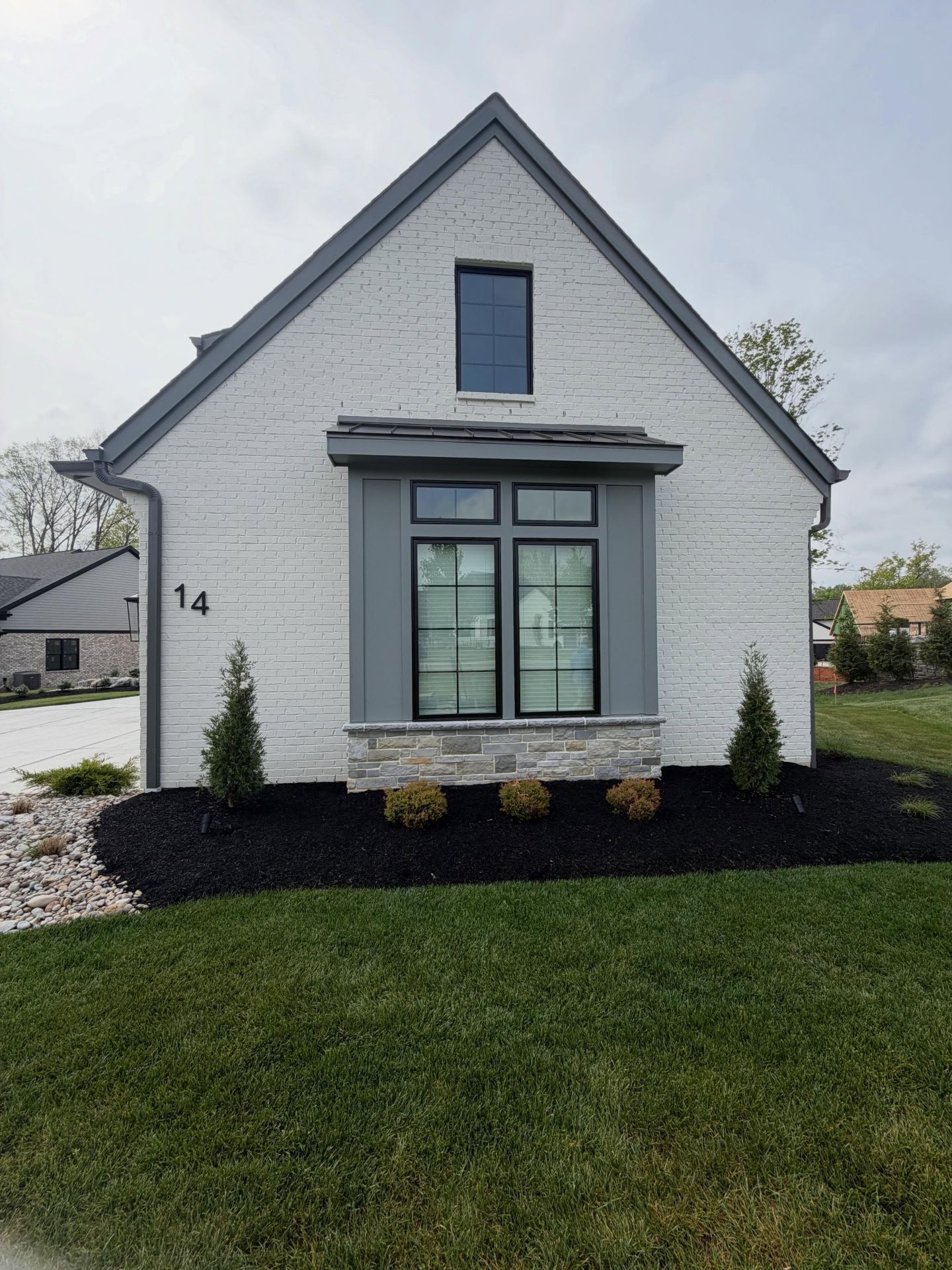 Gray house with black trim, front window, and number 14 beside a green lawn and mulch bed