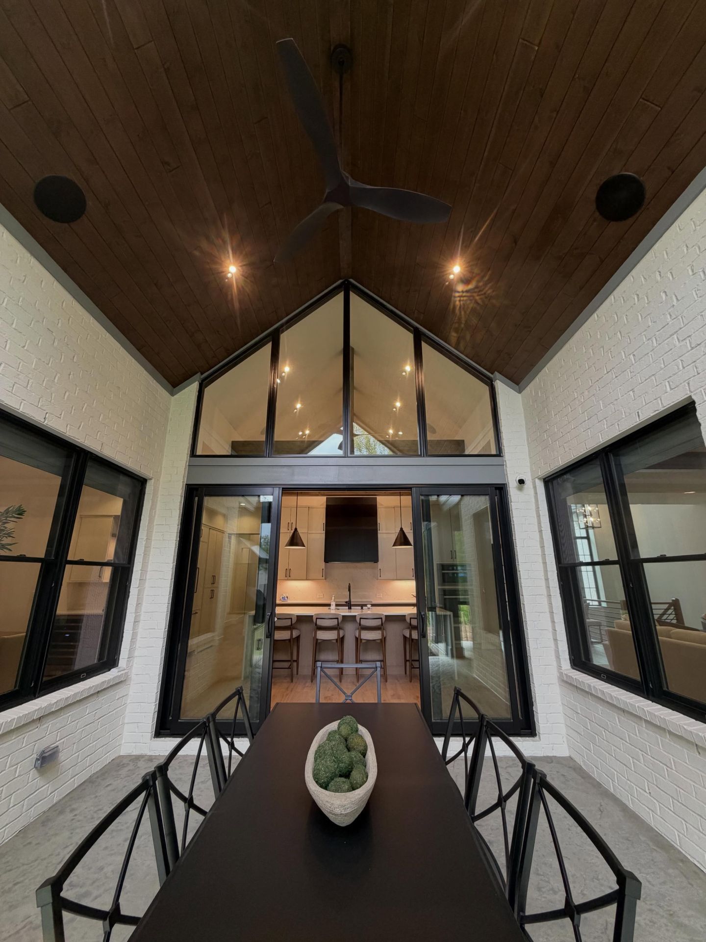 Modern enclosed patio with black dining table, chairs, wood ceiling, and glass doors to an interior room