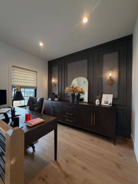 Modern home office with dark wood cabinets, desk, window blinds, and light hardwood floors.
