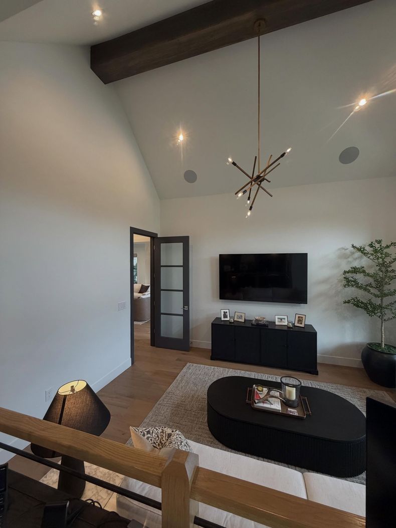 Modern living room with wall-mounted TV, black coffee table, beige sofa, and large windows.