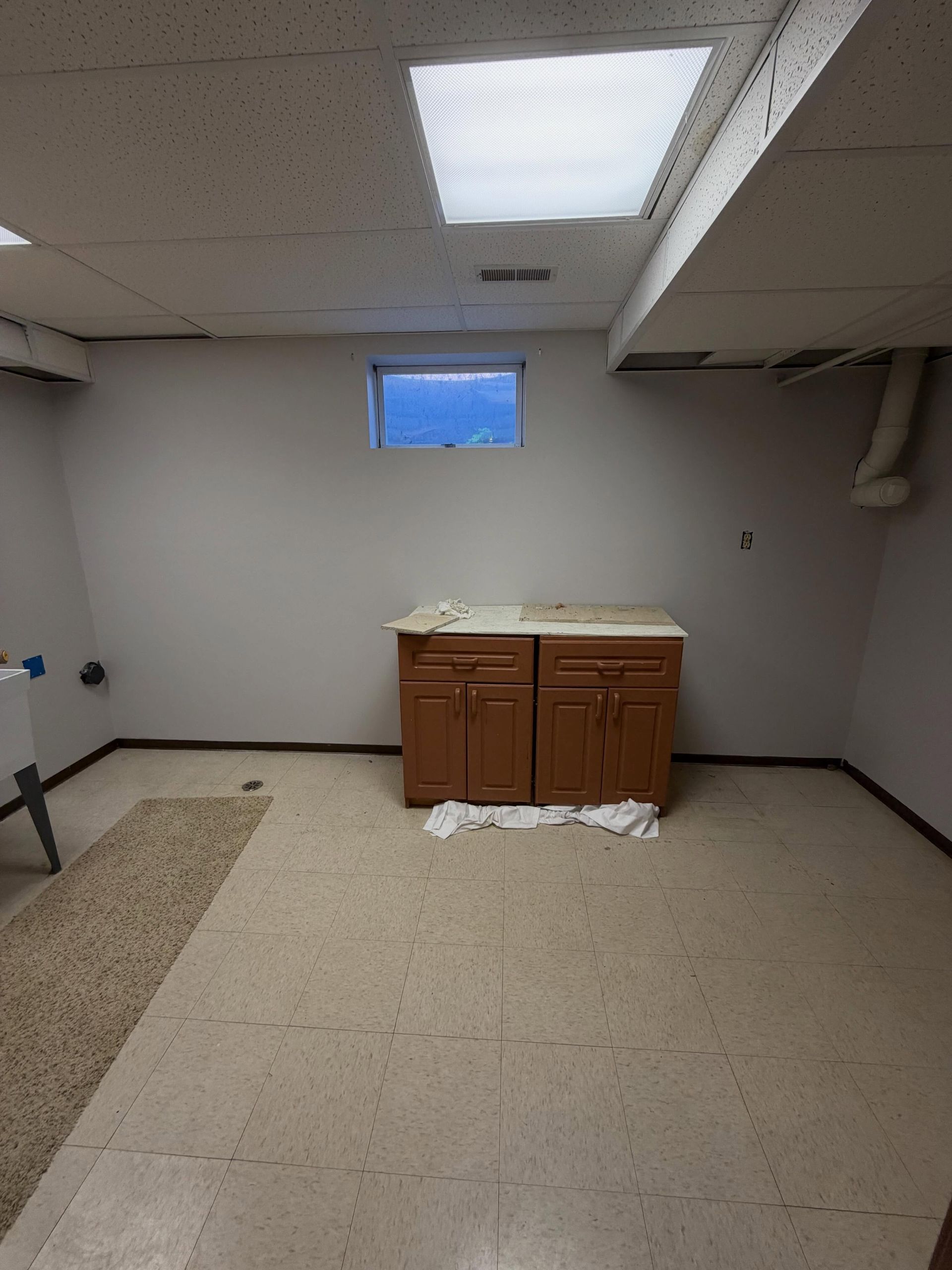 Empty basement laundry area with washer hookups and a small cabinet under a window.