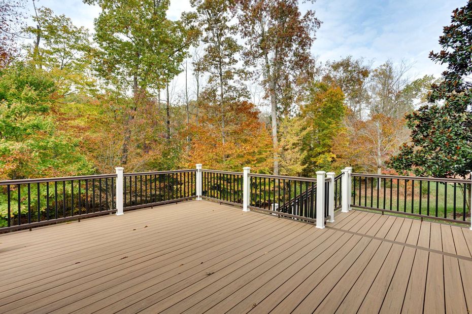 Wooden deck with black railing overlooking autumn trees and a green lawn