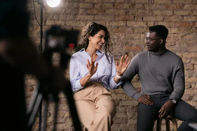 A man and a woman are sitting next to each other in front of a camera.