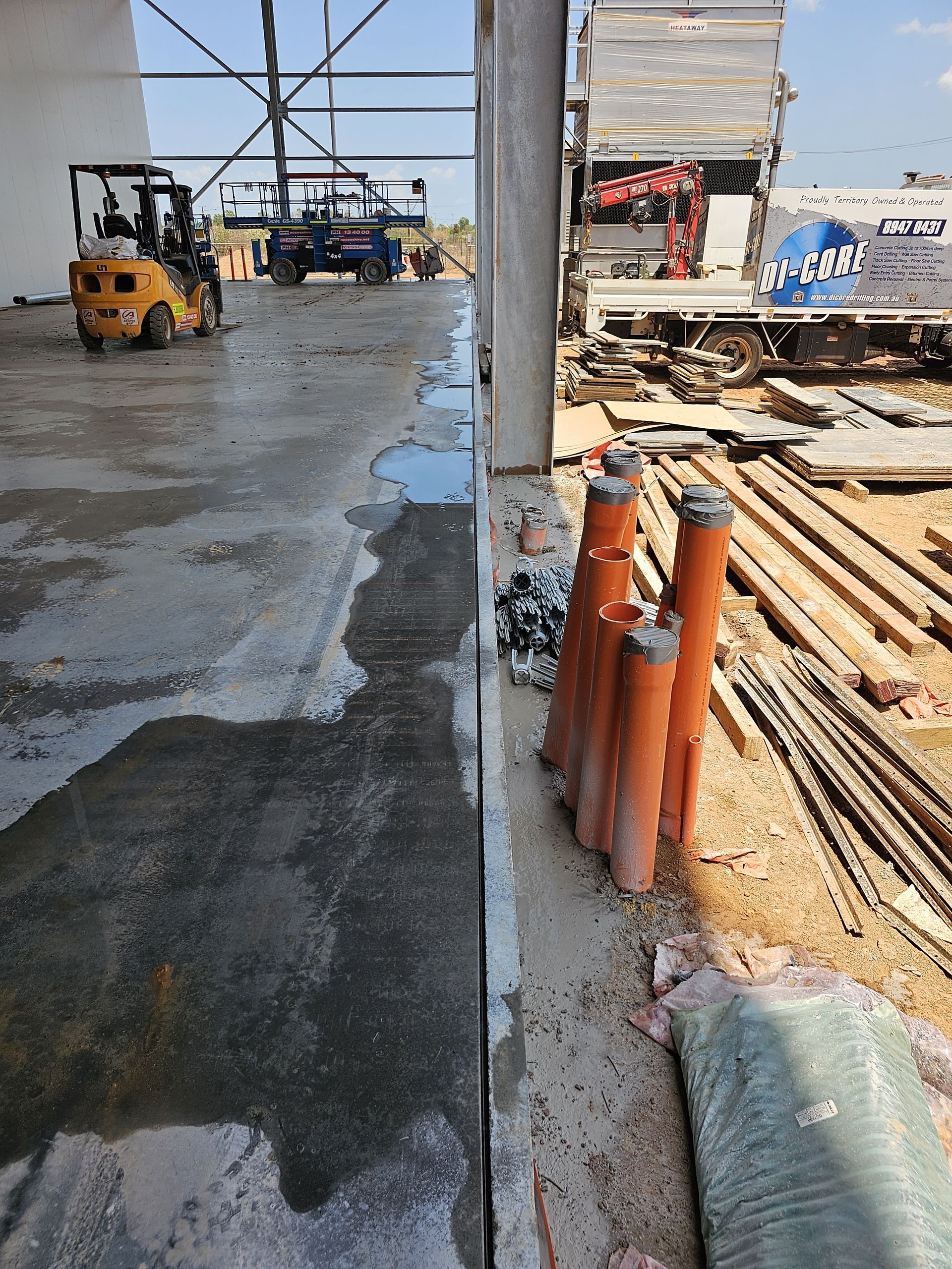 Construction site with a wet concrete floor, orange pipes, and construction equipment - — Di-Core Drilling and Cutting in Katherine, NT
