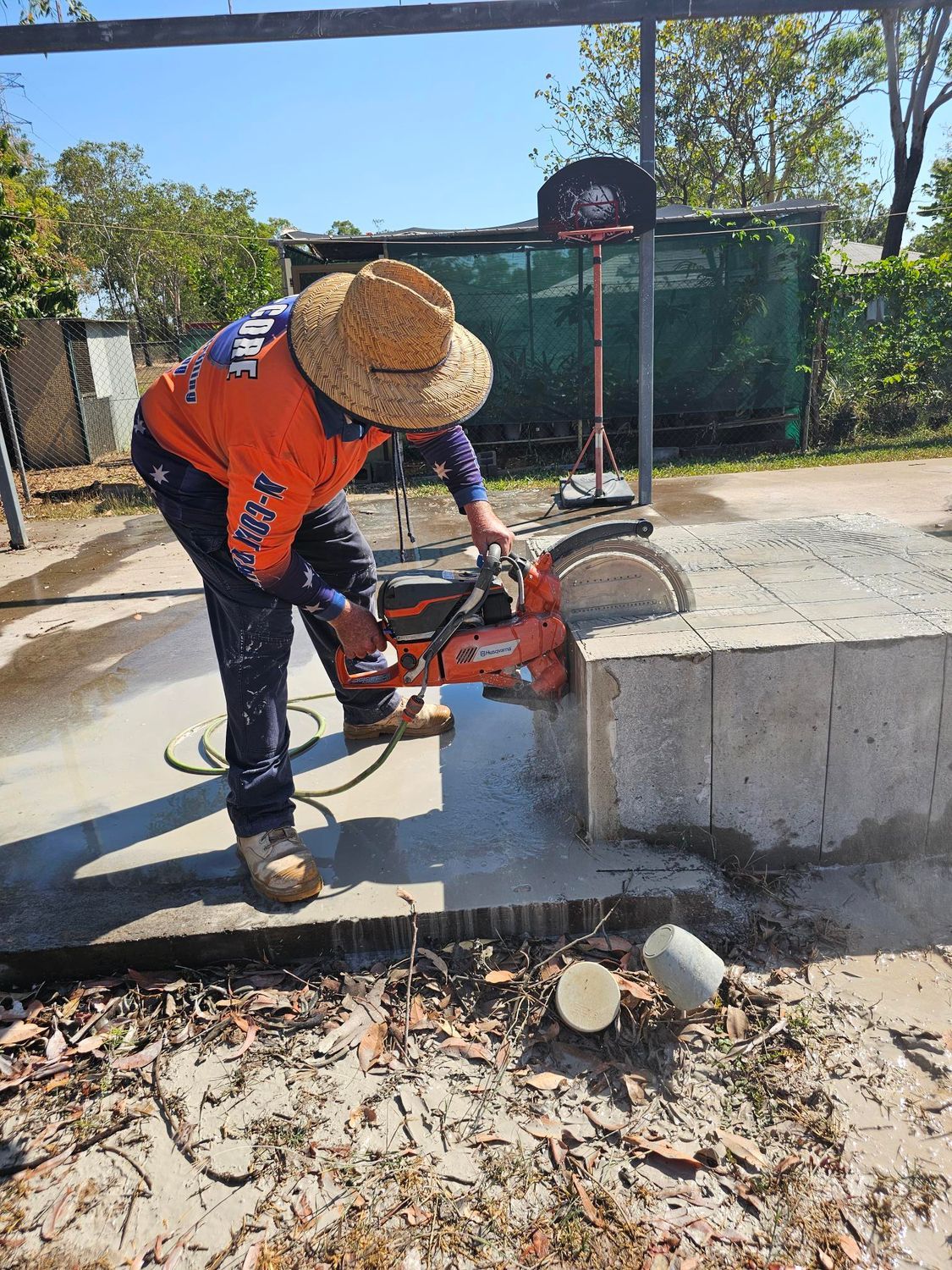 A worker in orange shirt cuts concrete block with a saw outdoors — Di-Core Drilling and Cutting in Darwin, NT