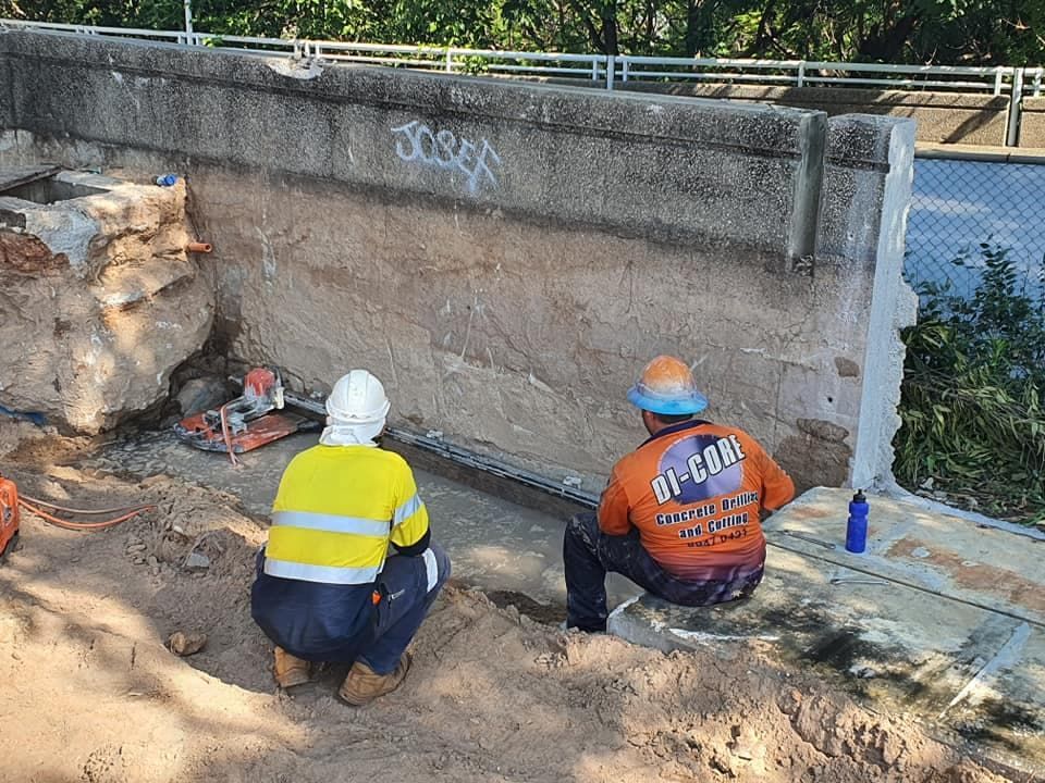 Two Construction Workers Are Kneeling in the Dirt Next to a Wall — Di-Core Drilling and Cutting in Darwin, NT
