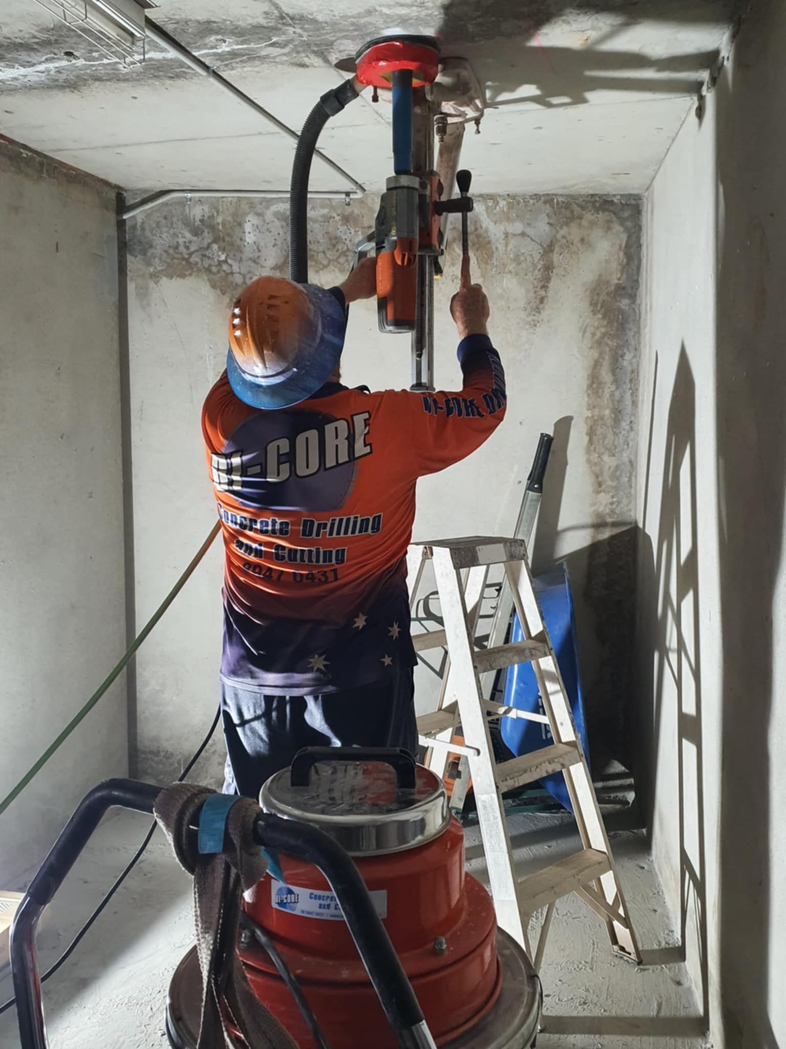 A Man in an Orange Shirt is Working on a Machine — Di-Core Drilling and Cutting in Darwin, NT