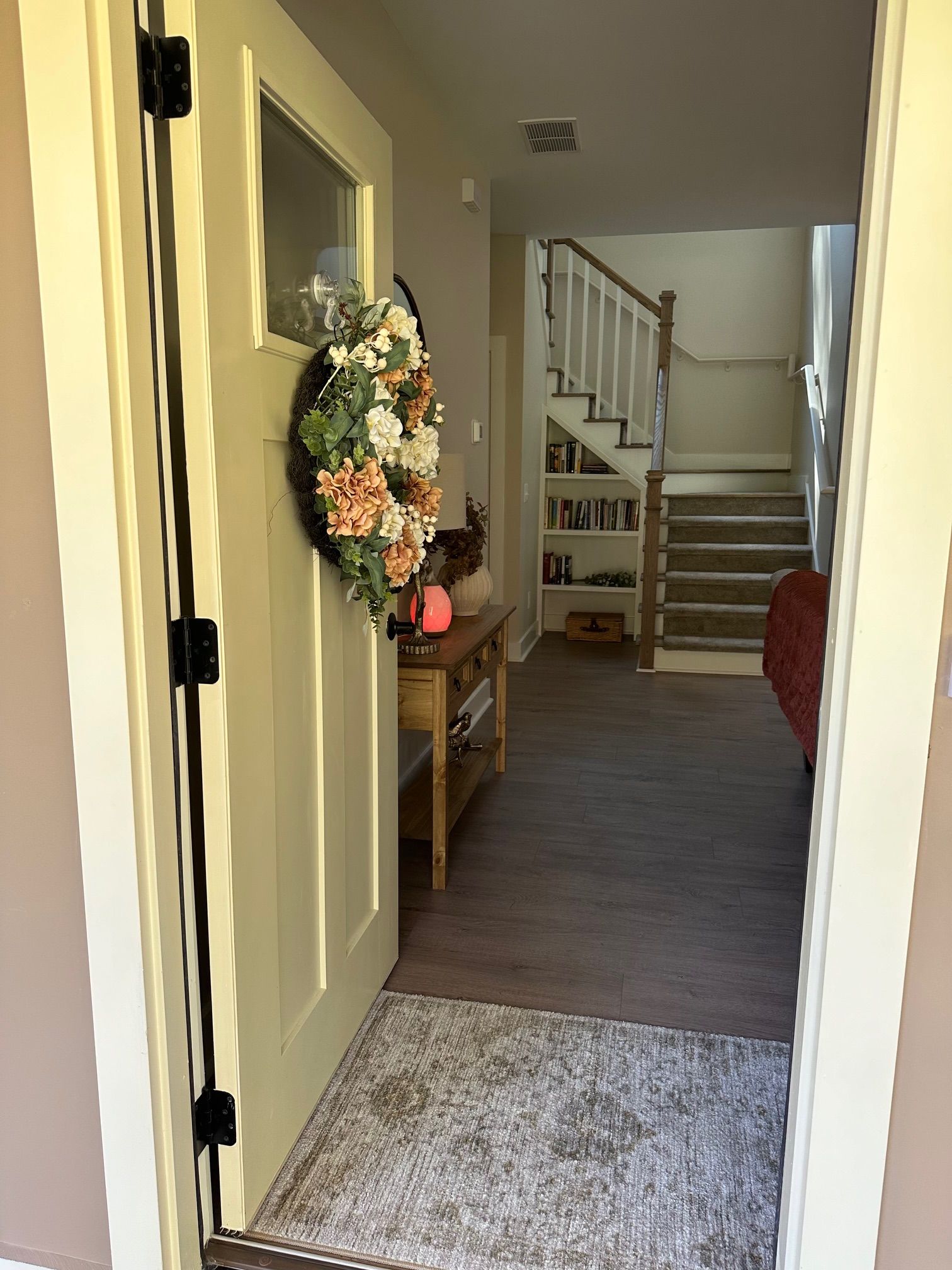 A door with a wreath on it is open to a living room with stairs.