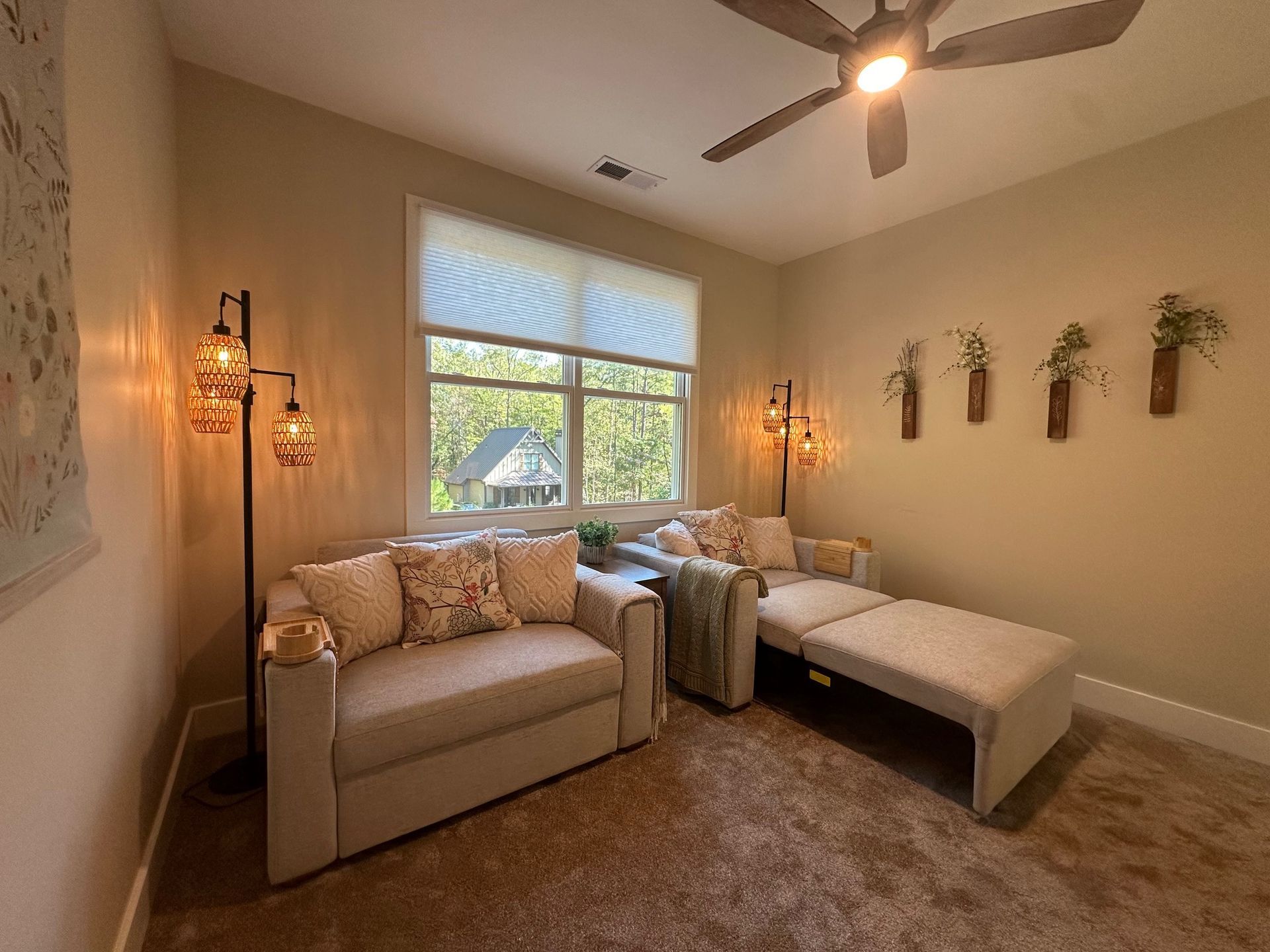 A living room with a couch , chair , ottoman and ceiling fan.