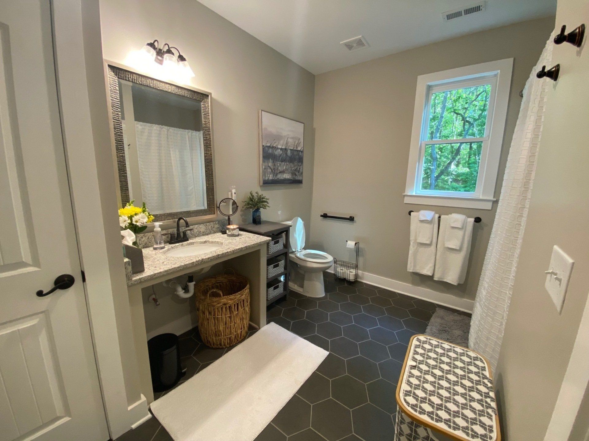 A bathroom with a toilet , sink , mirror and window.