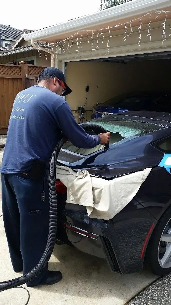 Man cleaning a black car with a vacuum hose outside a garage.