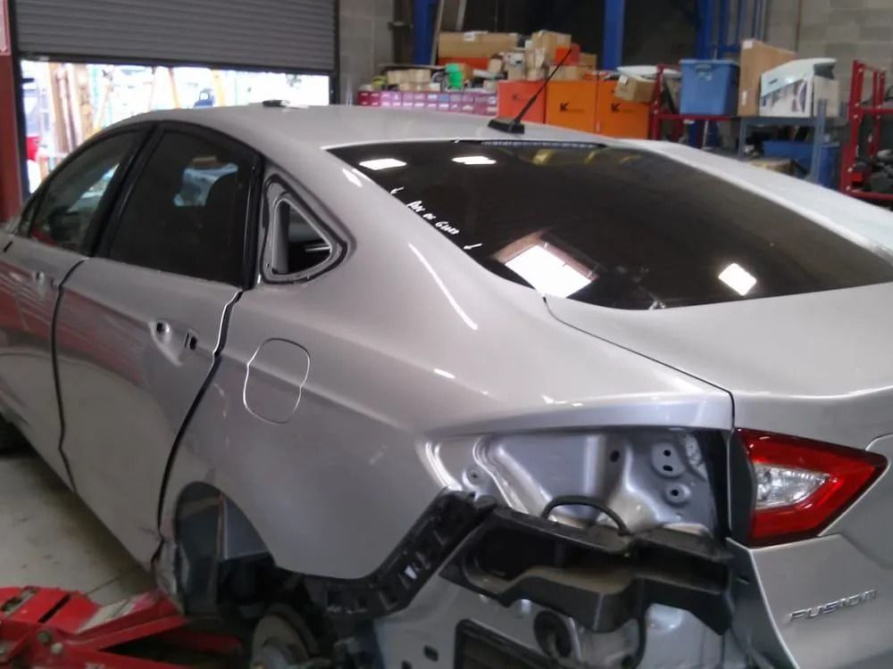 Silver car in auto repair shop with rear body panel removed.