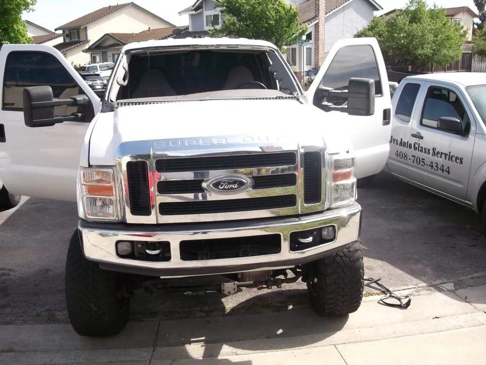 White Ford truck with open doors, parked in a driveway. Reflective chrome grill and large tires.