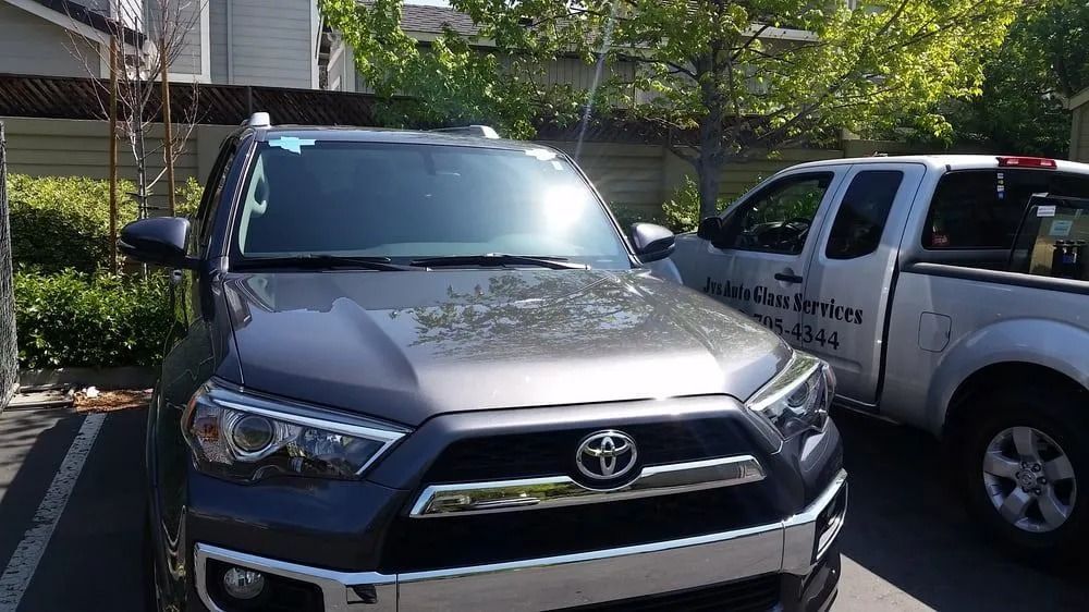 Gray Toyota 4Runner parked next to a white pickup truck. Sunny outdoor setting.