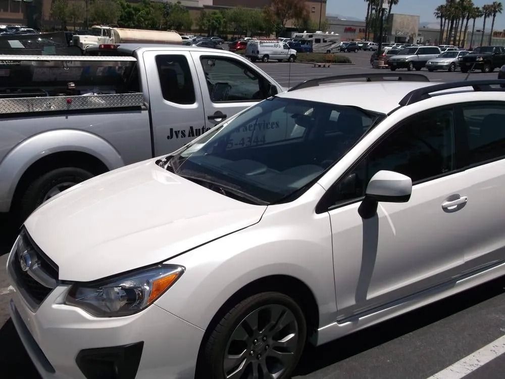 White Subaru Impreza parked next to a white truck in a parking lot. Sunny day.