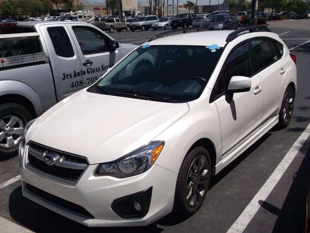 White Subaru Impreza hatchback parked in a parking lot. The windshield has blue tape on it.
