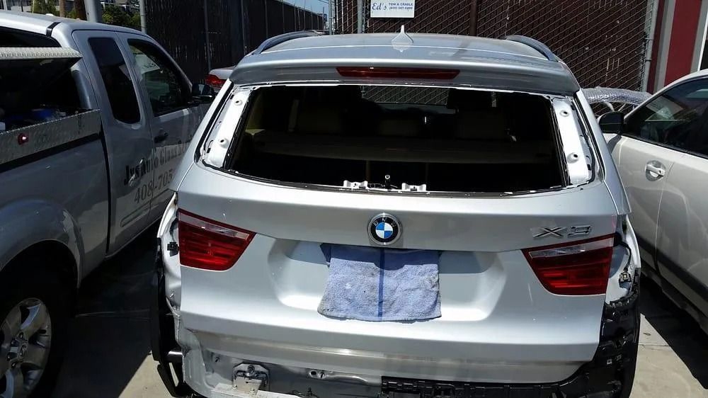 Silver BMW SUV with rear window missing, damaged bumper, outdoors.