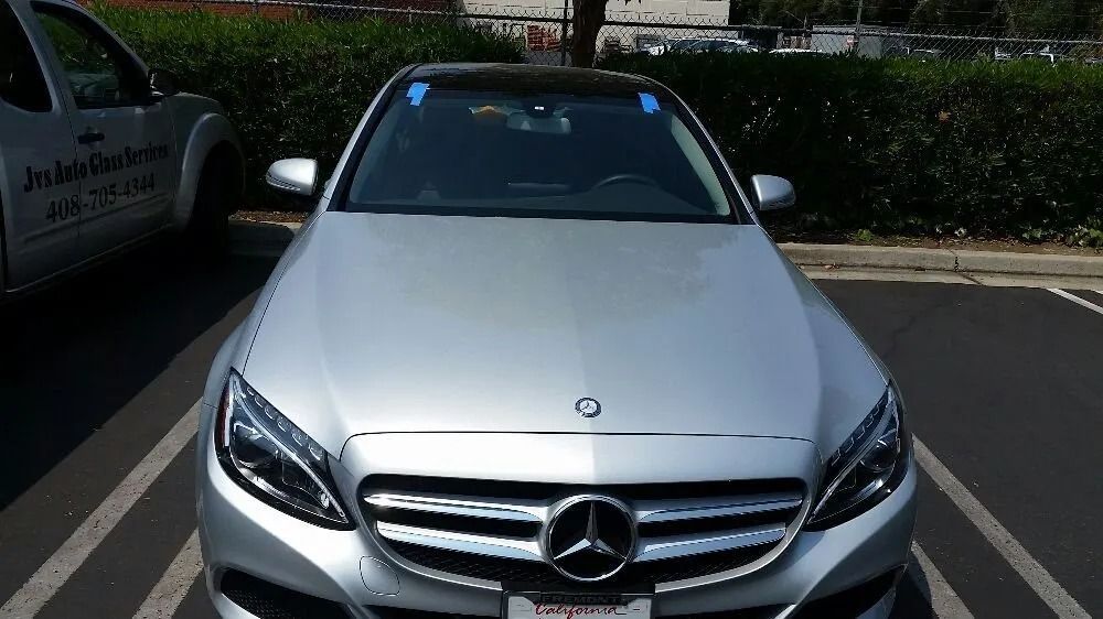 Silver Mercedes sedan parked in a parking lot, with a service truck visible on the left.