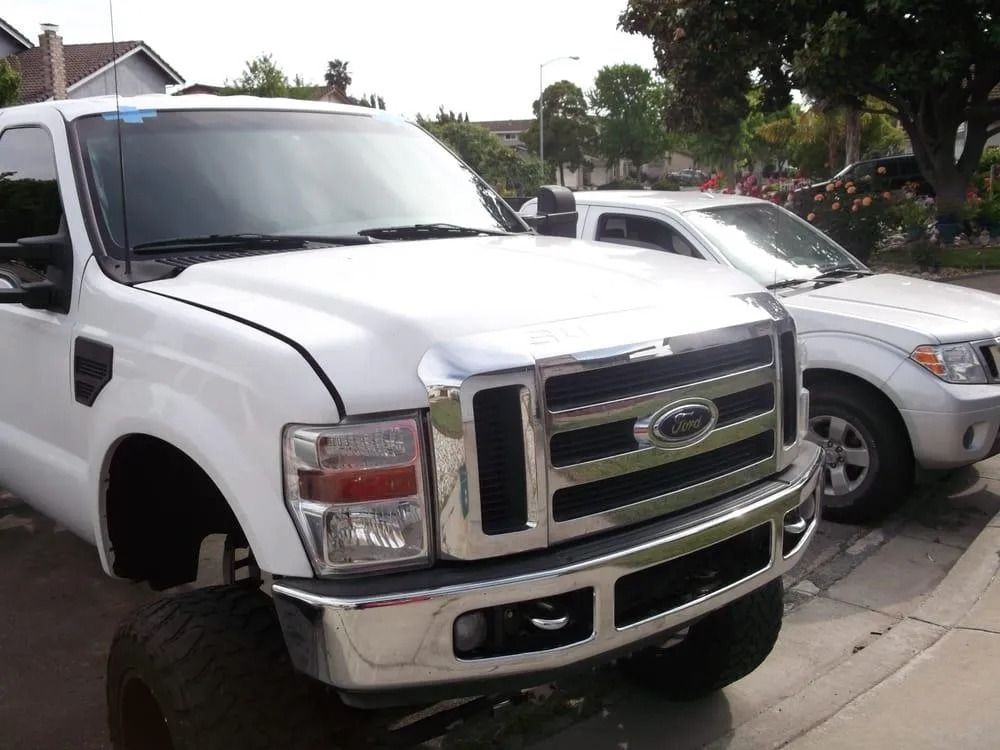 White Ford truck parked next to a silver car on a street in front of a house.