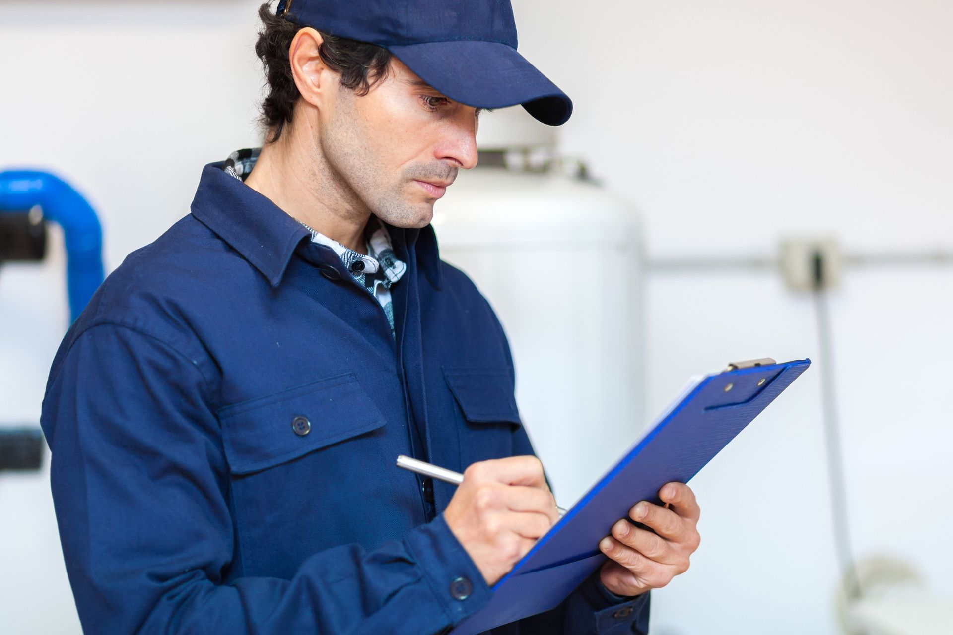 A man in a blue uniform is holding a clipboard and writing on it.