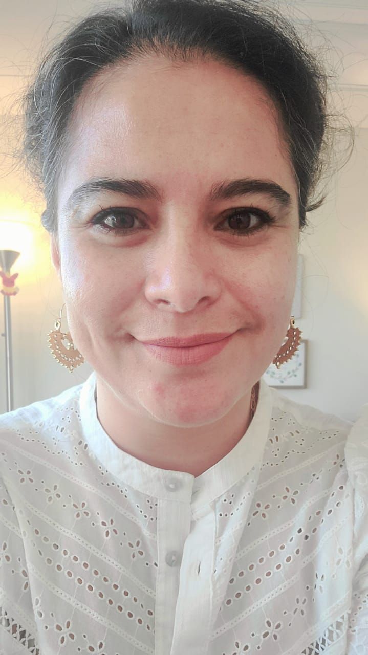 A woman wearing a white shirt and earrings is smiling for the camera.