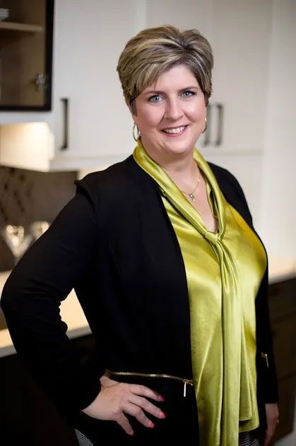 A woman wearing a black cardigan and a yellow shirt is standing in a kitchen.