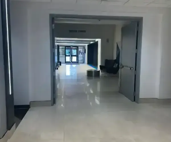 Hallway with open doors. Gray doors frame a long corridor leading to glass doors at the end.
