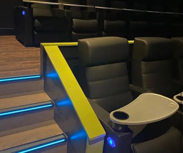 Movie theater seating with tiered rows, black leather recliners, yellow accents, and blue LED step lights.