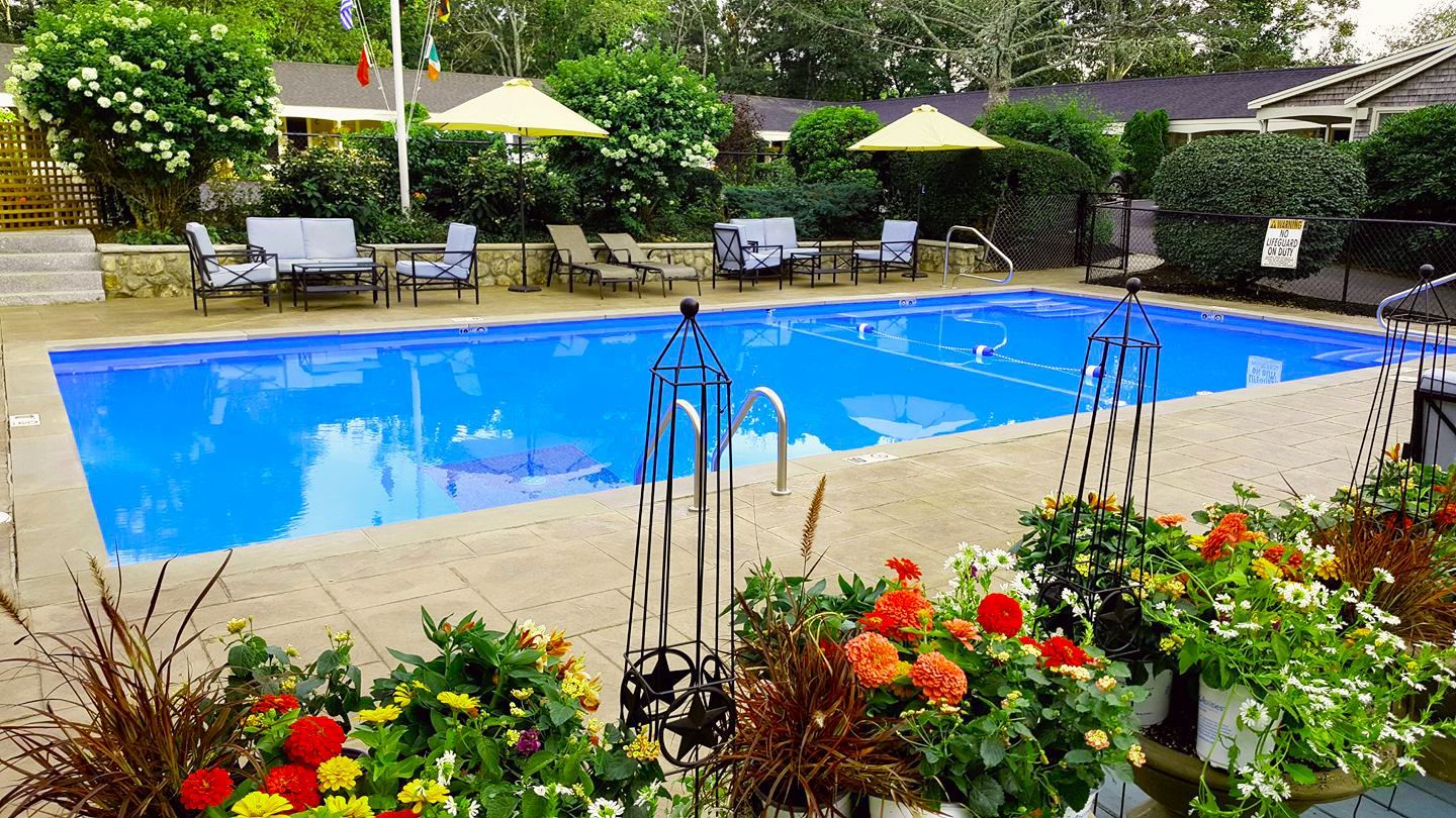 Pool with lounge chairs, umbrellas, and flowers in a courtyard setting.