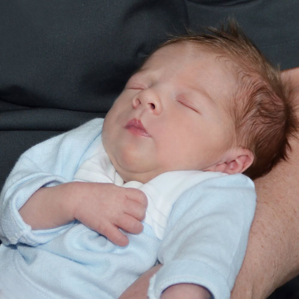 Een baby in een blauw shirt slaapt in iemands armen