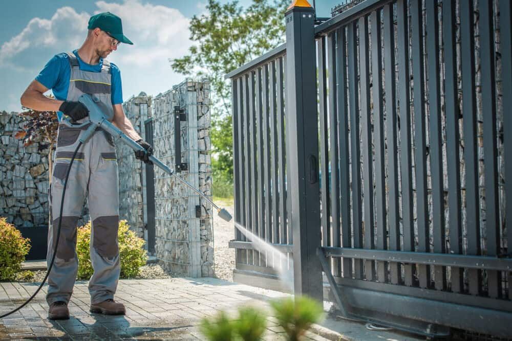 A Man is Using a High Pressure Washer to Clean a Fence — South Coast Pressure Washer in Shellharbour, NSW