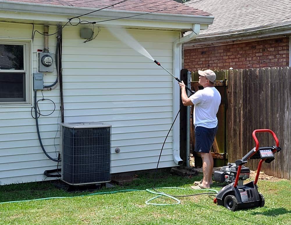 A Man is Using a High Pressure Washer to Clean the Side of a House — South Coast Pressure Washer in Nowra, NSW
