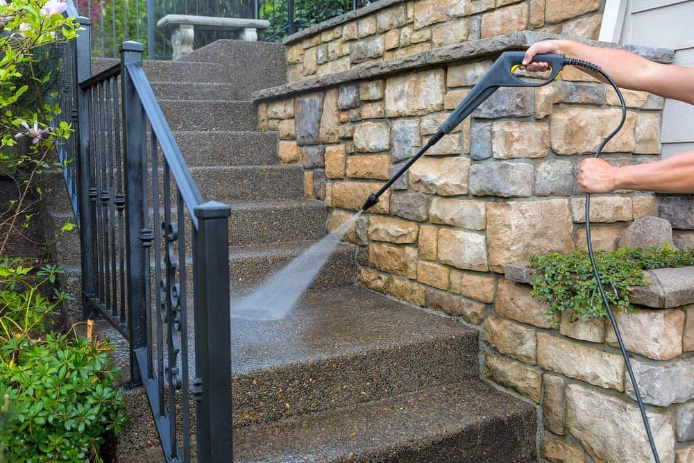 A Man is Using a High Pressure Washer to Clean the Steps of a Stone Wall — South Coast Pressure Washer in Albion Park, NSW