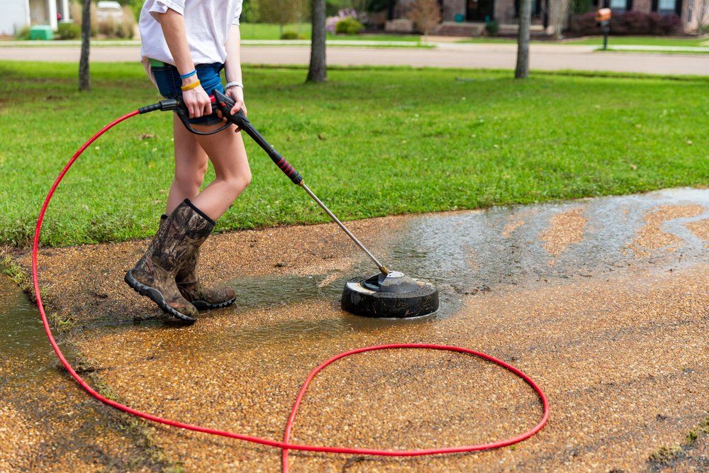 A Woman is Using a Pressure Washer to Clean a Driveway — South Coast Pressure Washer in Shellharbour, NSW