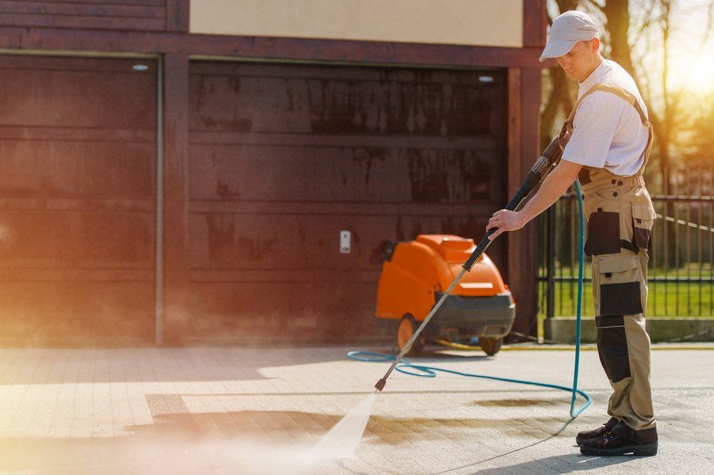 A Man is Using a High Pressure Washer to Clean a Driveway — South Coast Pressure Washer in Nowra, NSW