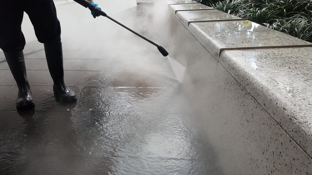 A Person is Using a High Pressure Washer to Clean a Sidewalk — South Coast Pressure Washer in Warilla, NSW