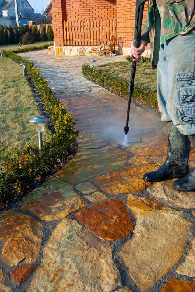 A Man is Cleaning a Stone Walkway With a High Pressure Washer — South Coast Pressure Washer in Kiama, NSW