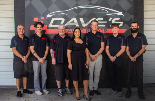 Dave's Auto Repair team standing in front of their shop sign.  Men and a woman pose in uniforms, shop logo visible.