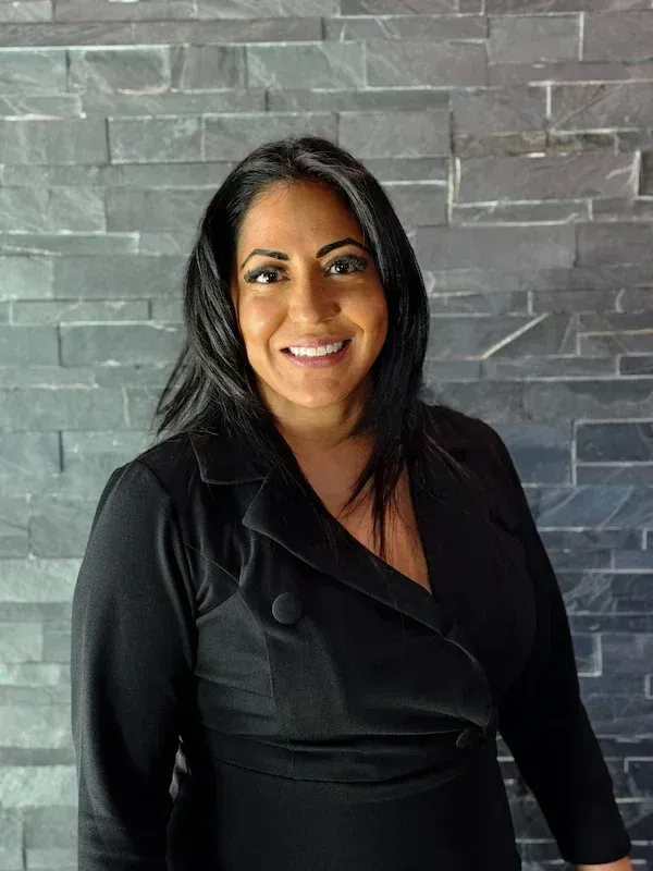 Woman smiling, wearing black jacket, against a grey stone wall backdrop. | Dave's Auto Repair