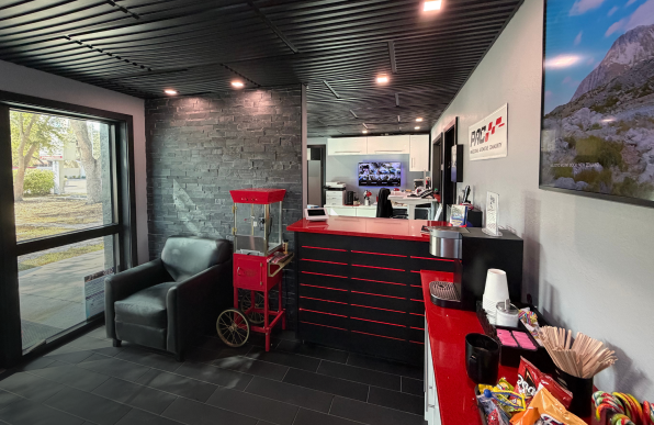 Lobby with a black and red reception desk, popcorn machine, and snacks. Black ceiling, a large window, and a gray brick wall. | Dave's Auto Repair