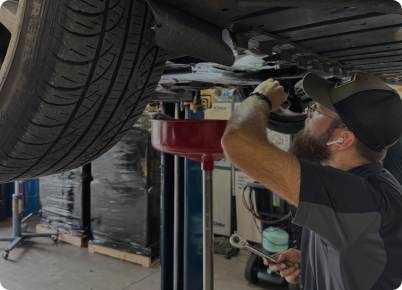 Mechanic working under a car on a lift, changing oil. A red oil pan is in place. | Dave's Auto Repair