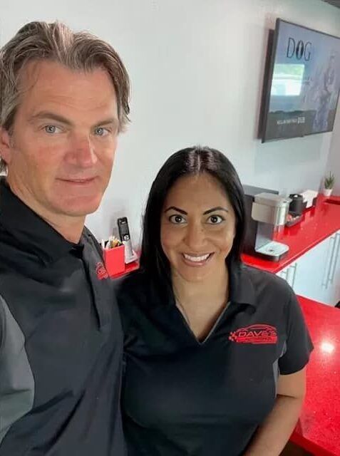 Two people in black polo shirts smile in a red-accented office. | Dave's Auto Repair