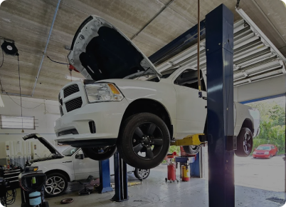 White pickup truck raised on a lift inside a garage, hood open. Another car in the background. | Dave's Auto Repair