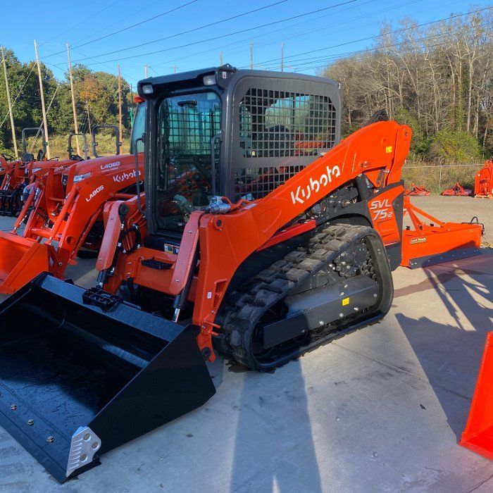 Orange Kubota track skid steer loader with bucket and a rear attachment on a concrete surface.
