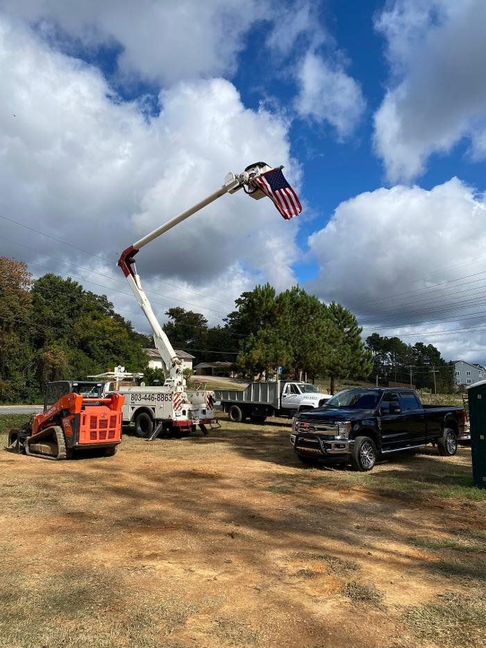 Cherry picker truck displaying an American flag against a partly cloudy sky with other vehicles in a field.